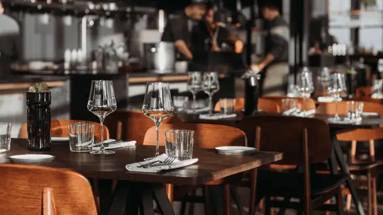 Salão de restaurante com mesas montadas com taças e talheres